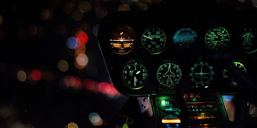 Illuminated aircraft dashboard dials against a blurred night city background.