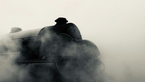 Close-up of a dark steam locomotive shrouded in drifting vapor