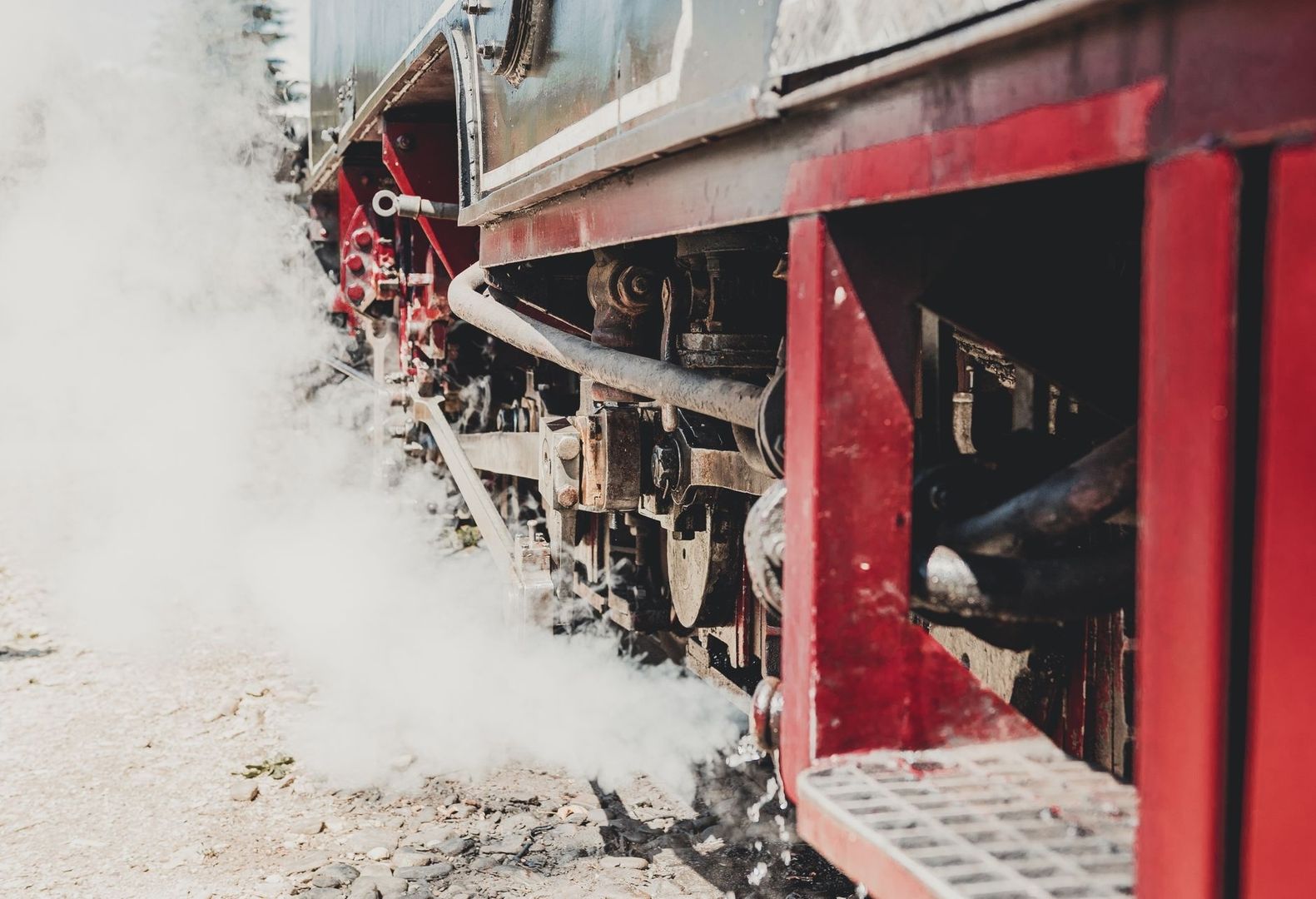 Close-up of a red steam locomotive chassis releasing white steam